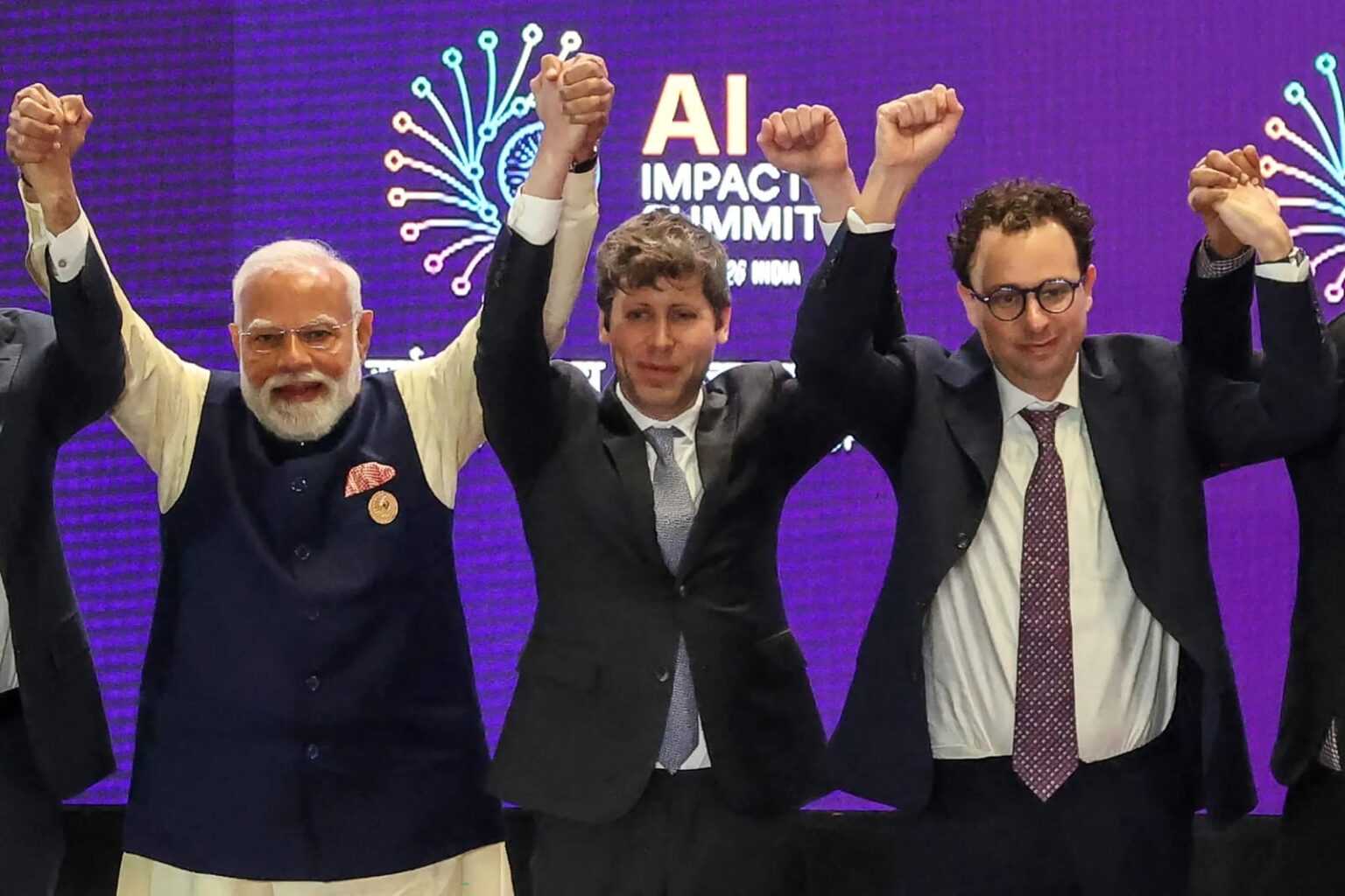 Indian Prime Minister Narendra Modi, OpenAI CEO Sam Altman, and Anthropic CEO Dario Amodei raising their arms on stage at the AI Impact Summit 2026 in New Delhi.